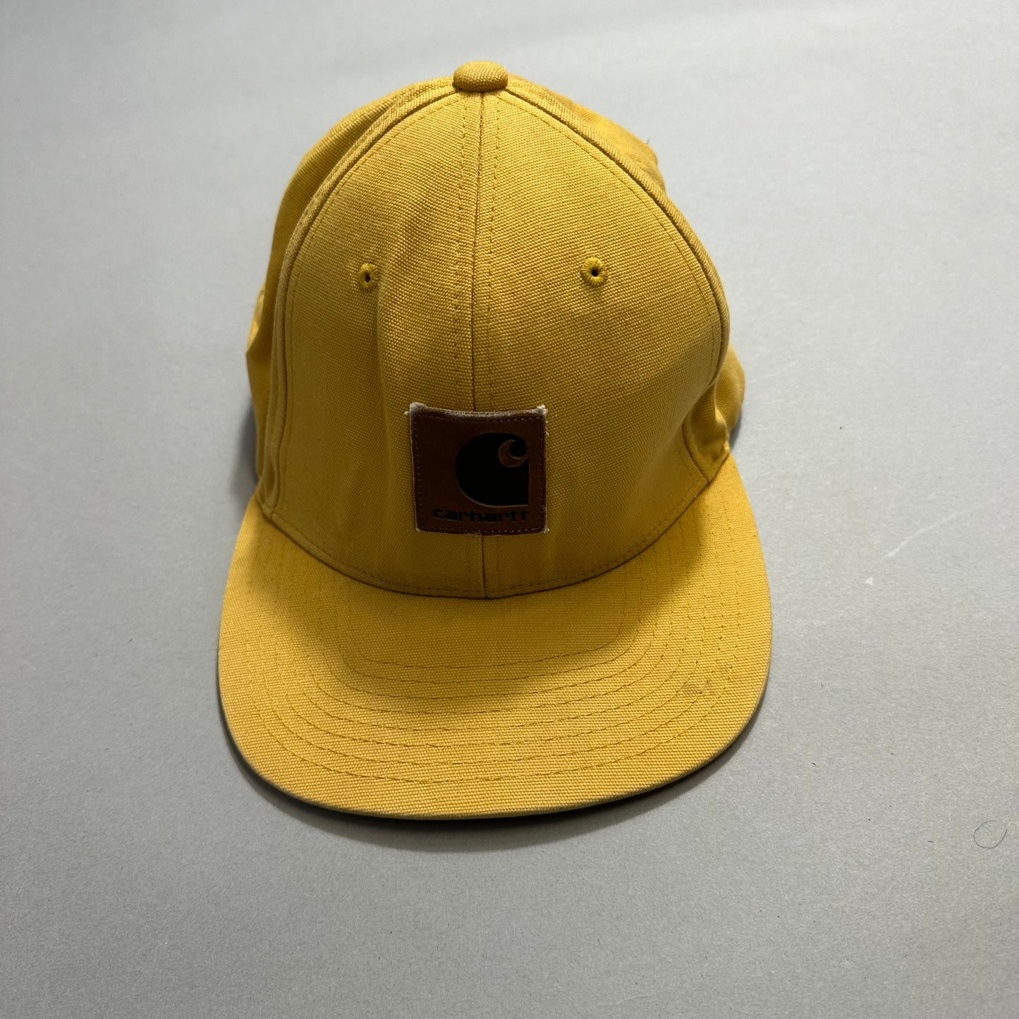 Yellow cap with a brown logo patch on gray background.