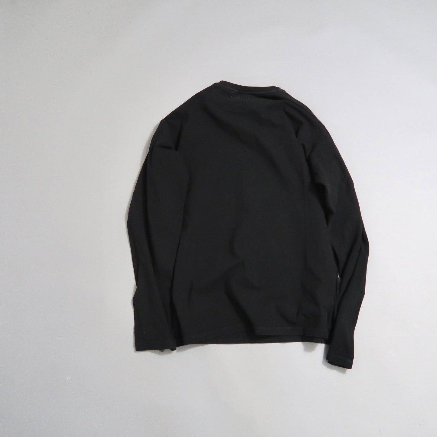 Black long-sleeve shirt laid flat on a light gray surface.