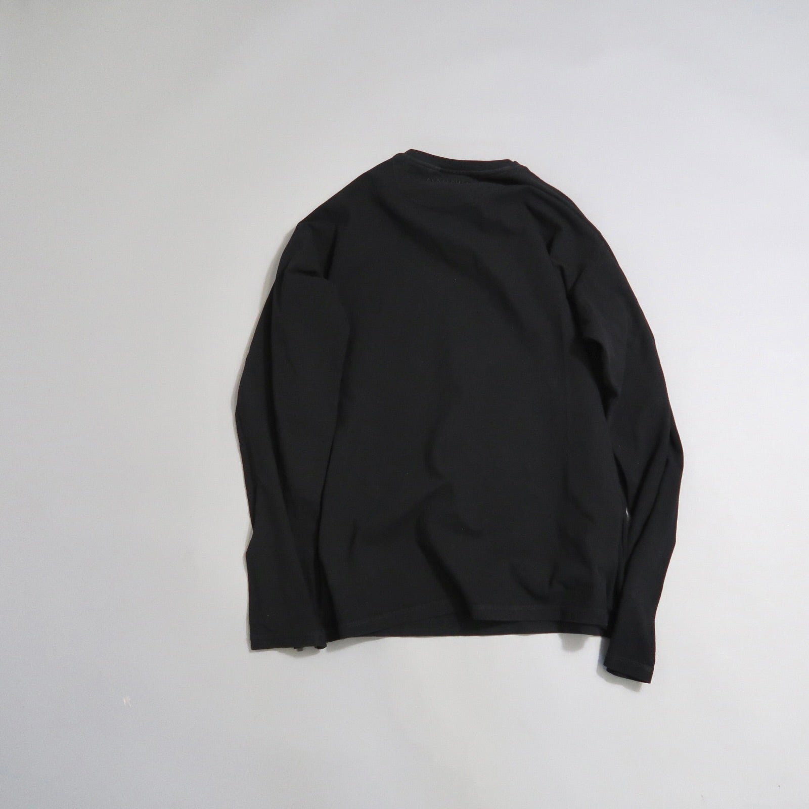 Black long-sleeve shirt laid flat on a light gray surface.