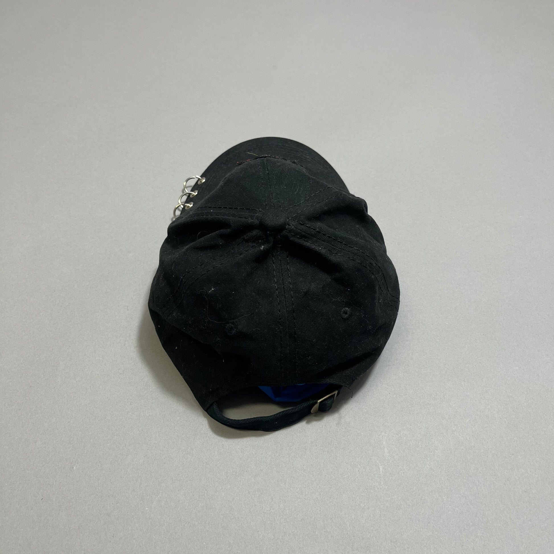 Black baseball cap with metal rings on a gray background.