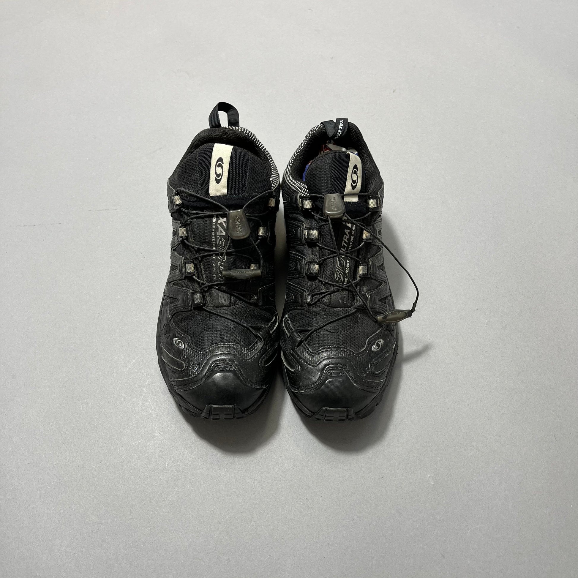 Pair of black trail running shoes on a gray surface.