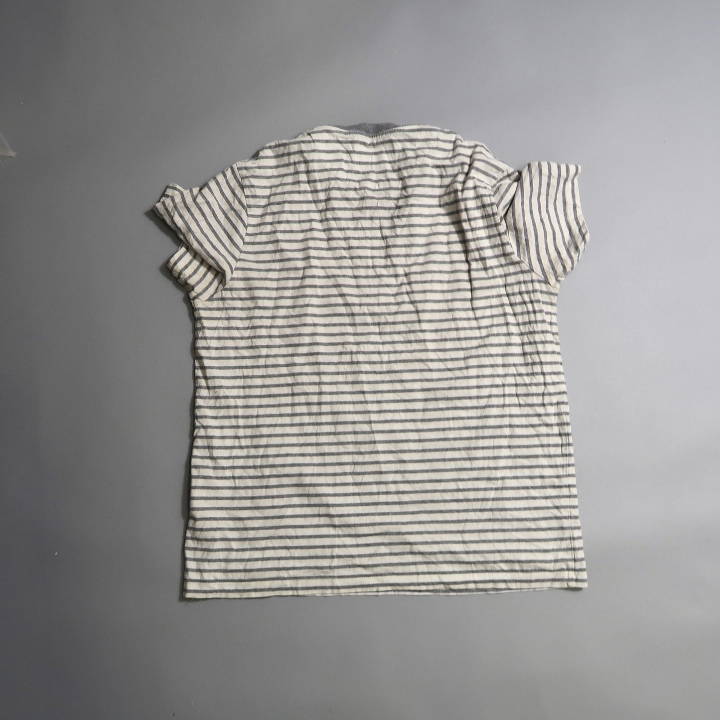Back view of a white T-shirt with black stripes on a gray background.