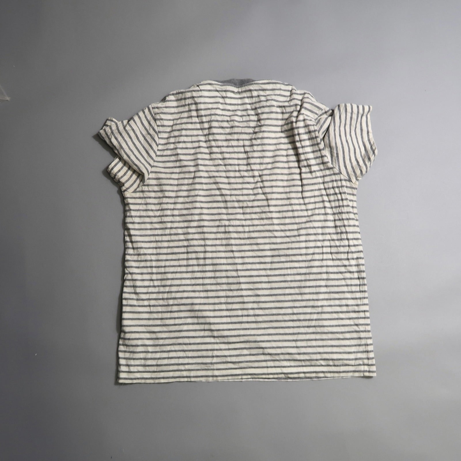 Back view of a white T-shirt with black stripes on a gray background.