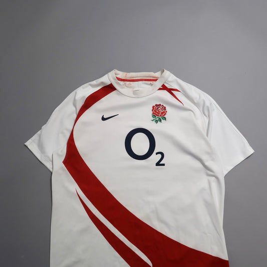 White rugby jersey with red design and rose emblem.