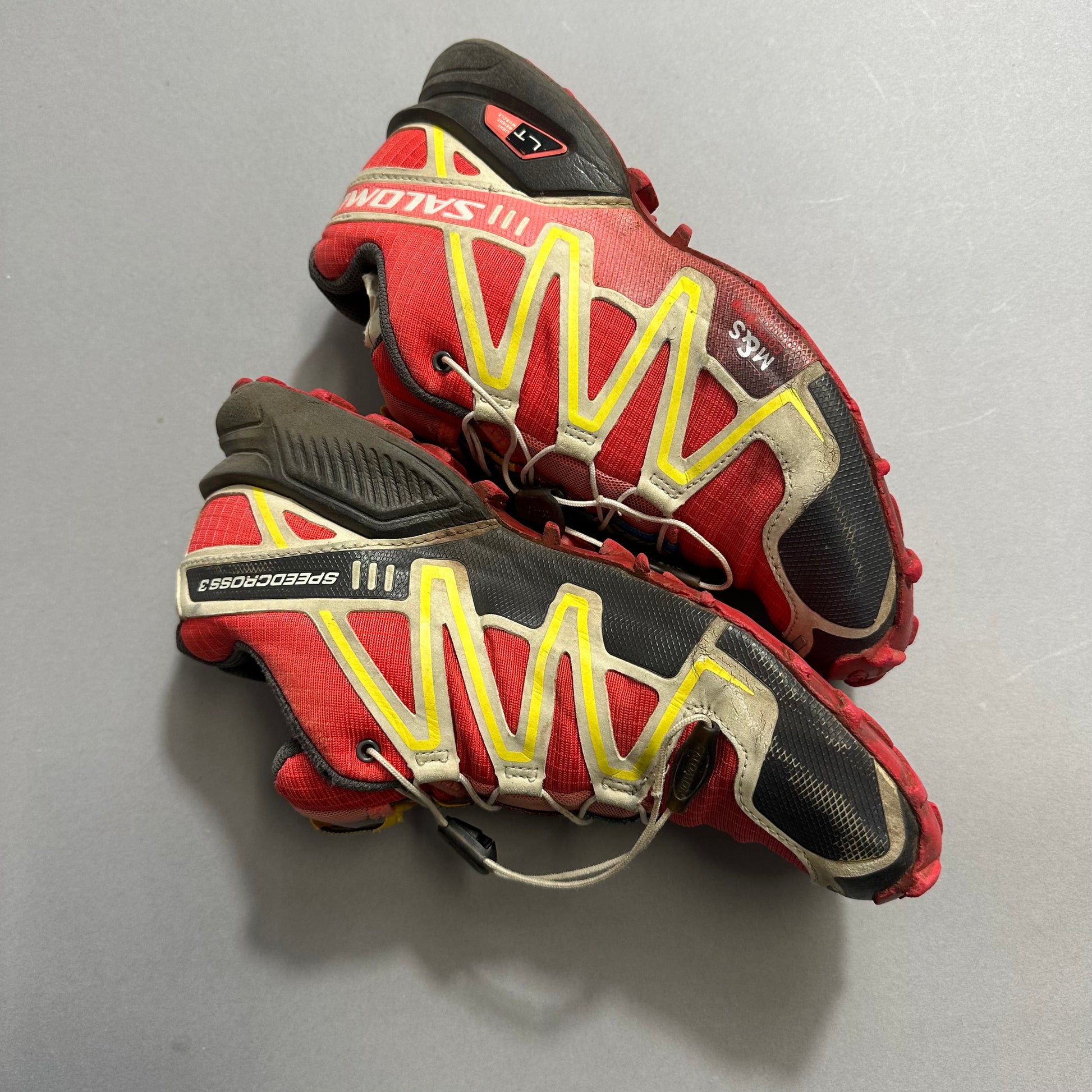 Red and black trail running shoes with yellow accents.