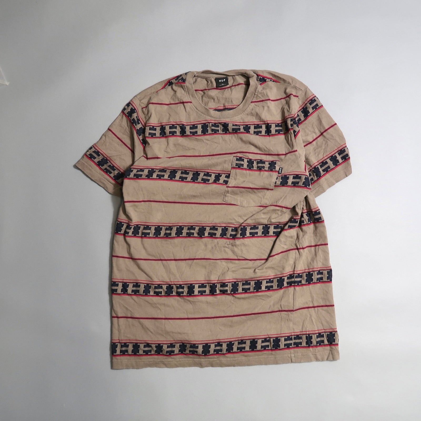 Beige T-shirt with red and navy geometric stripes on a flat surface.