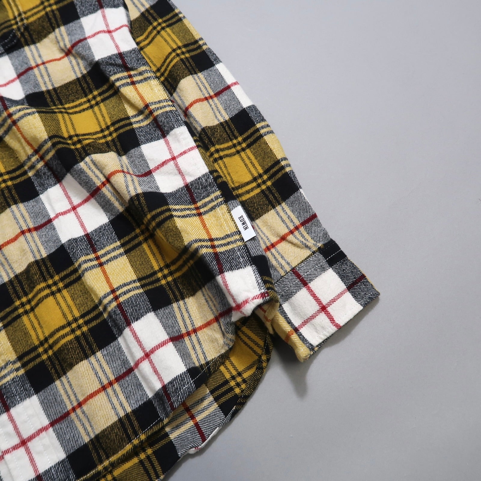 Yellow and black checkered fabric with a white tag on gray background.