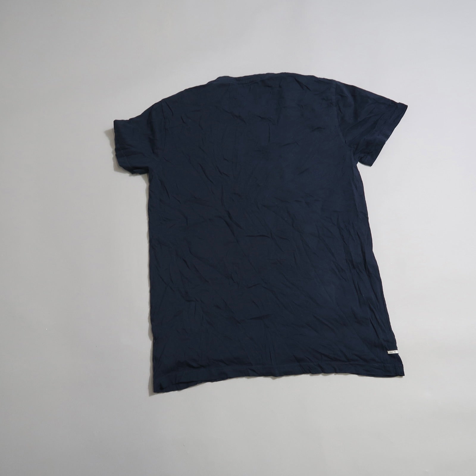 Wrinkled navy T-shirt laid flat on a plain surface.