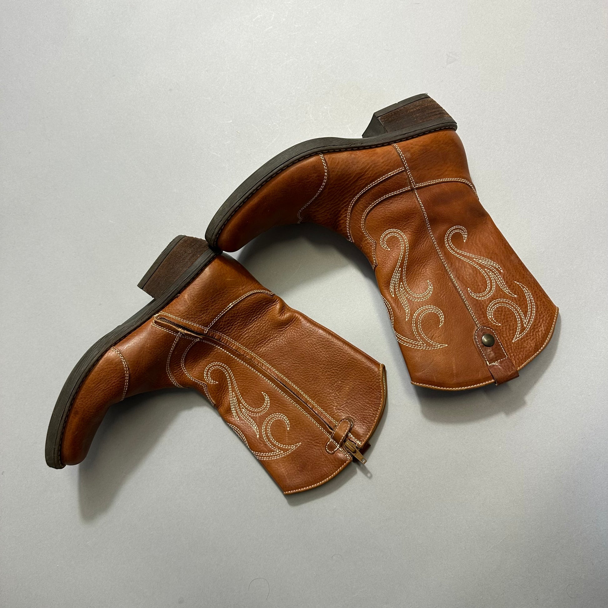 Brown cowboy boots with decorative stitching on a gray background.