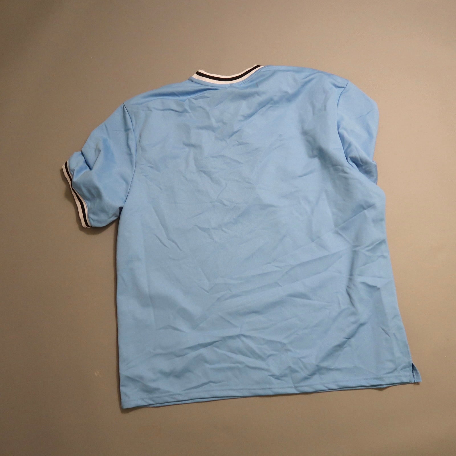 Wrinkled light blue T-shirt, rear view, on a flat surface.