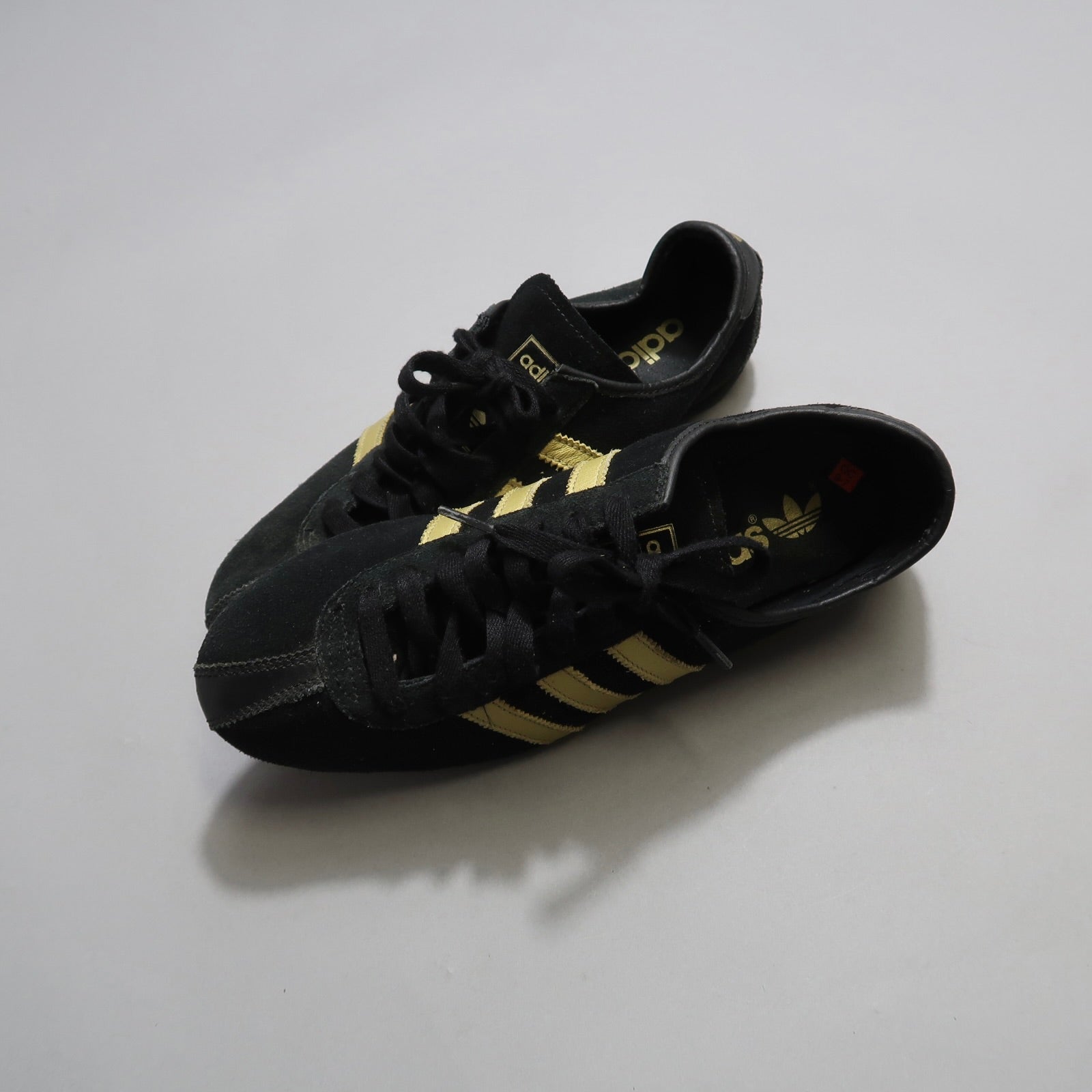 Black sneakers with gold stripes on a light gray background.