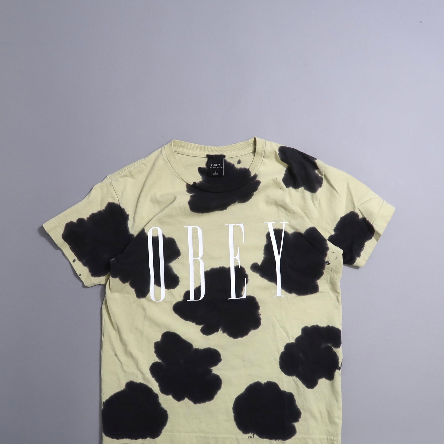 Beige t-shirt with black splotches and nullOBEYnull text in white.