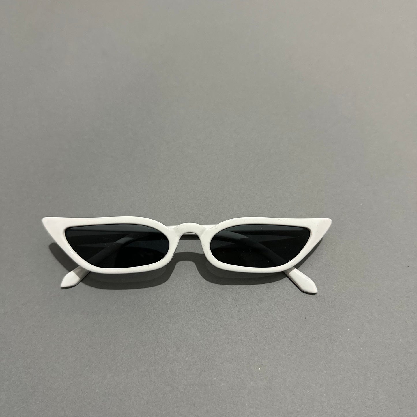 White cat-eye sunglasses on a gray background.