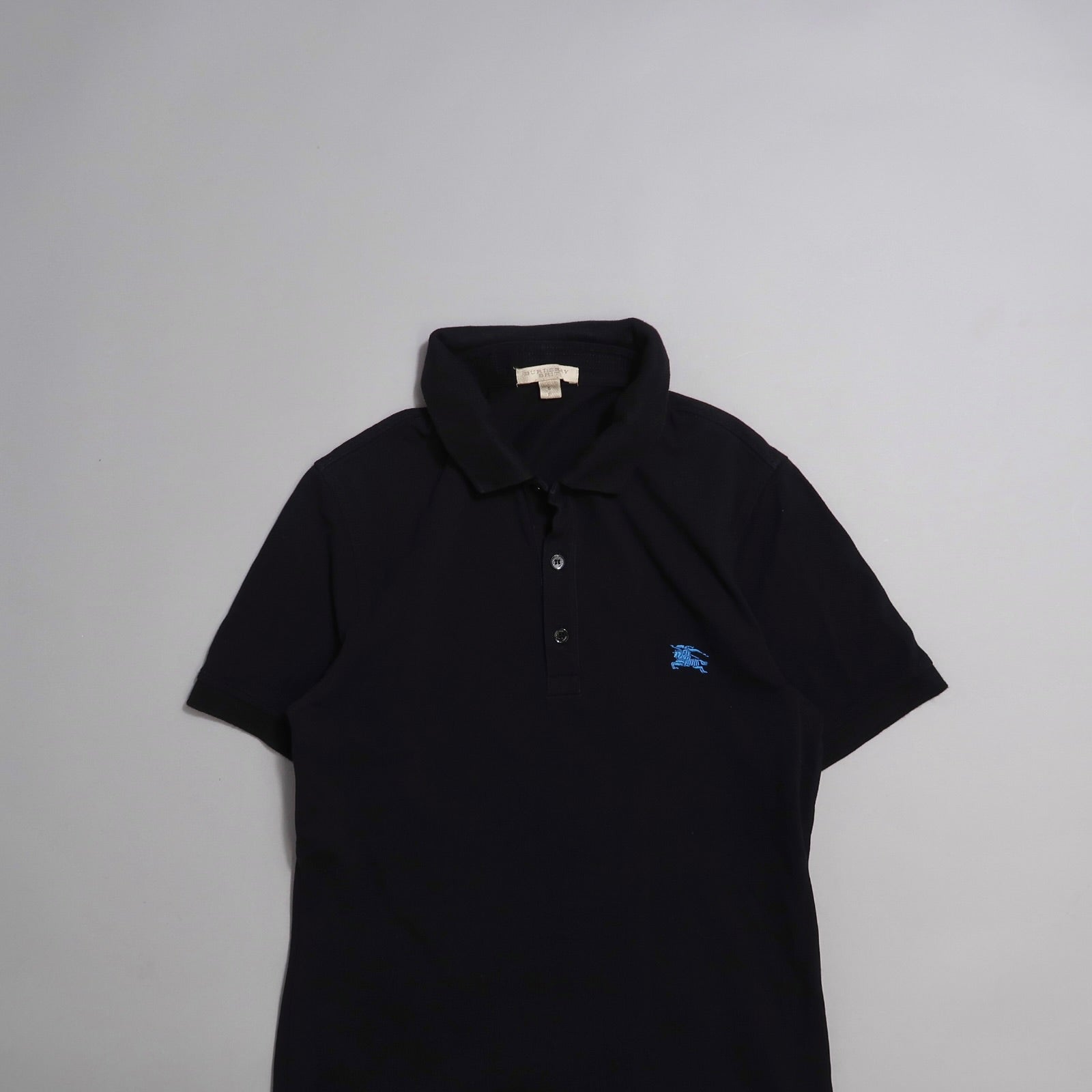 Black polo shirt with blue logo on chest, laid on a neutral background.