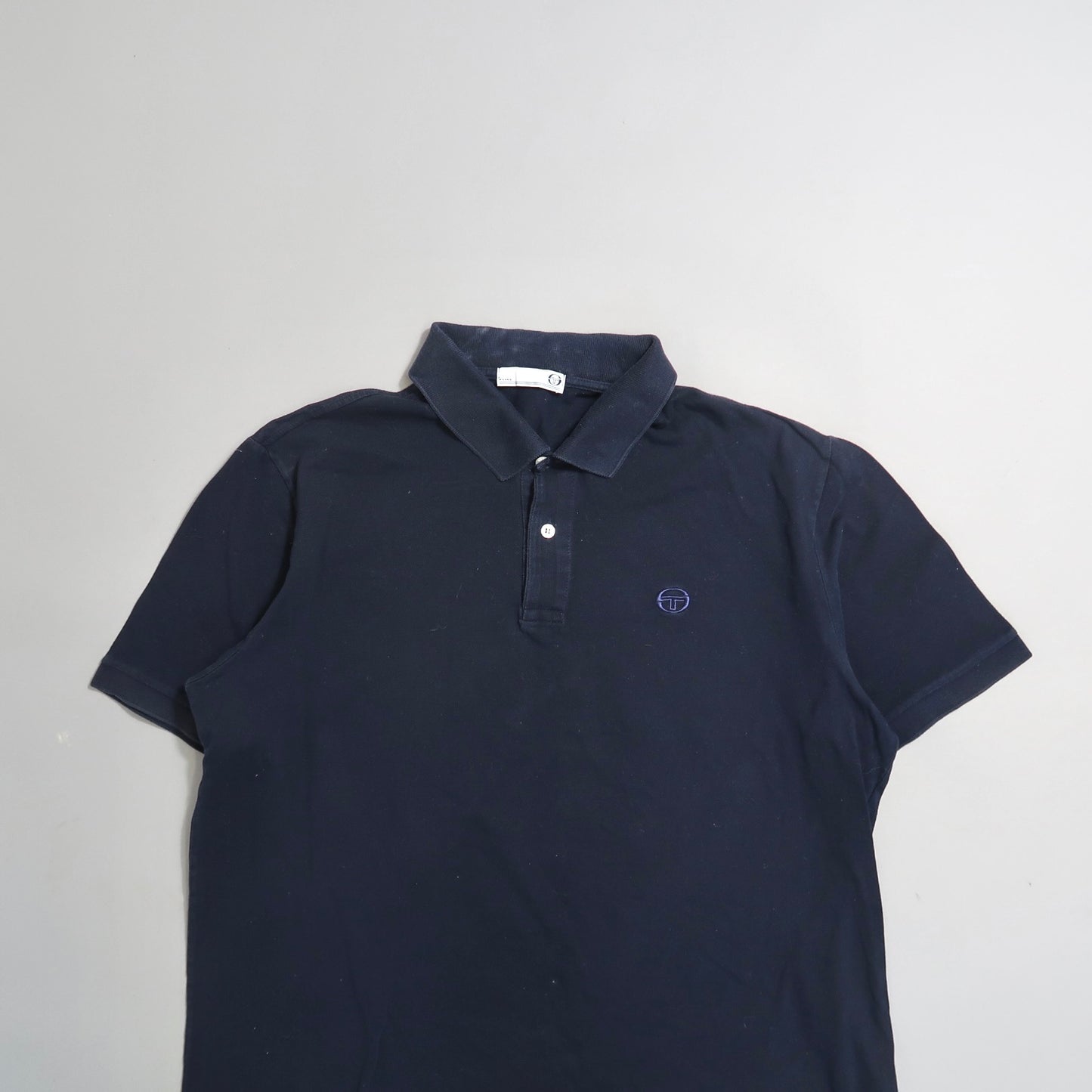 Navy blue polo shirt with a small logo on the chest, laid on a flat surface.