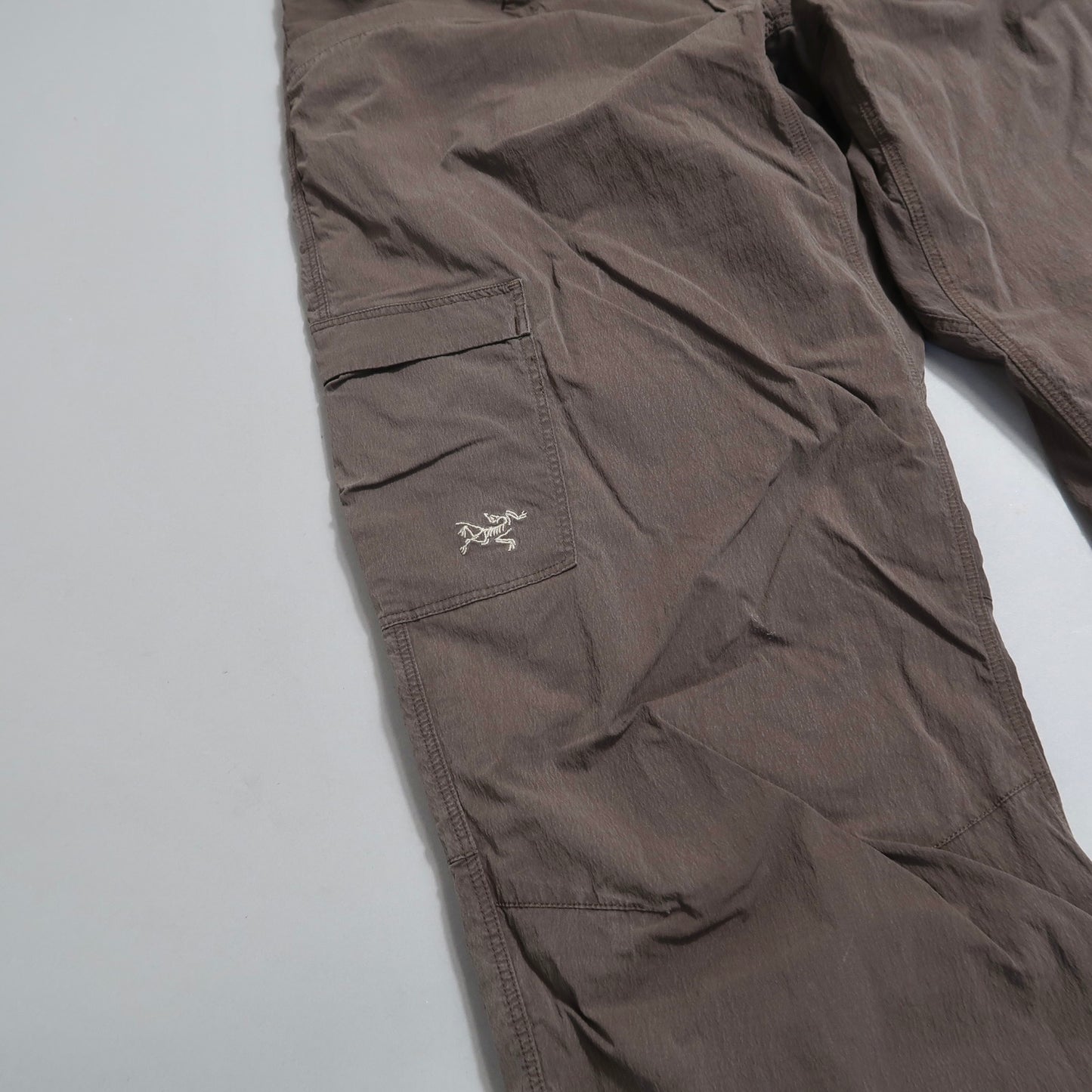 Brown cargo pants with a side pocket and small embroidered logo.