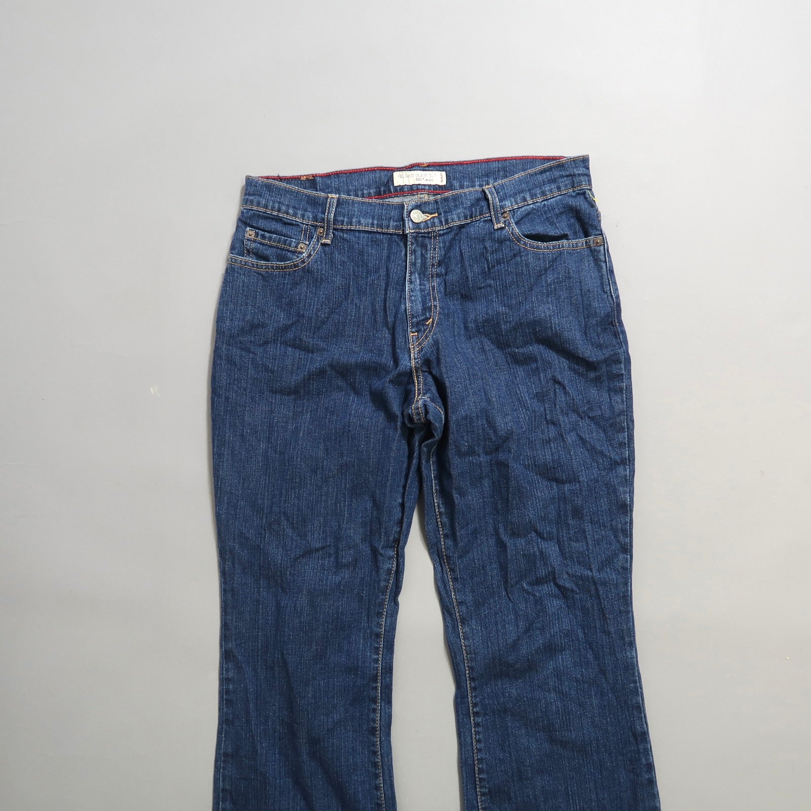 Blue denim jeans with a button and zip closure on a plain background.