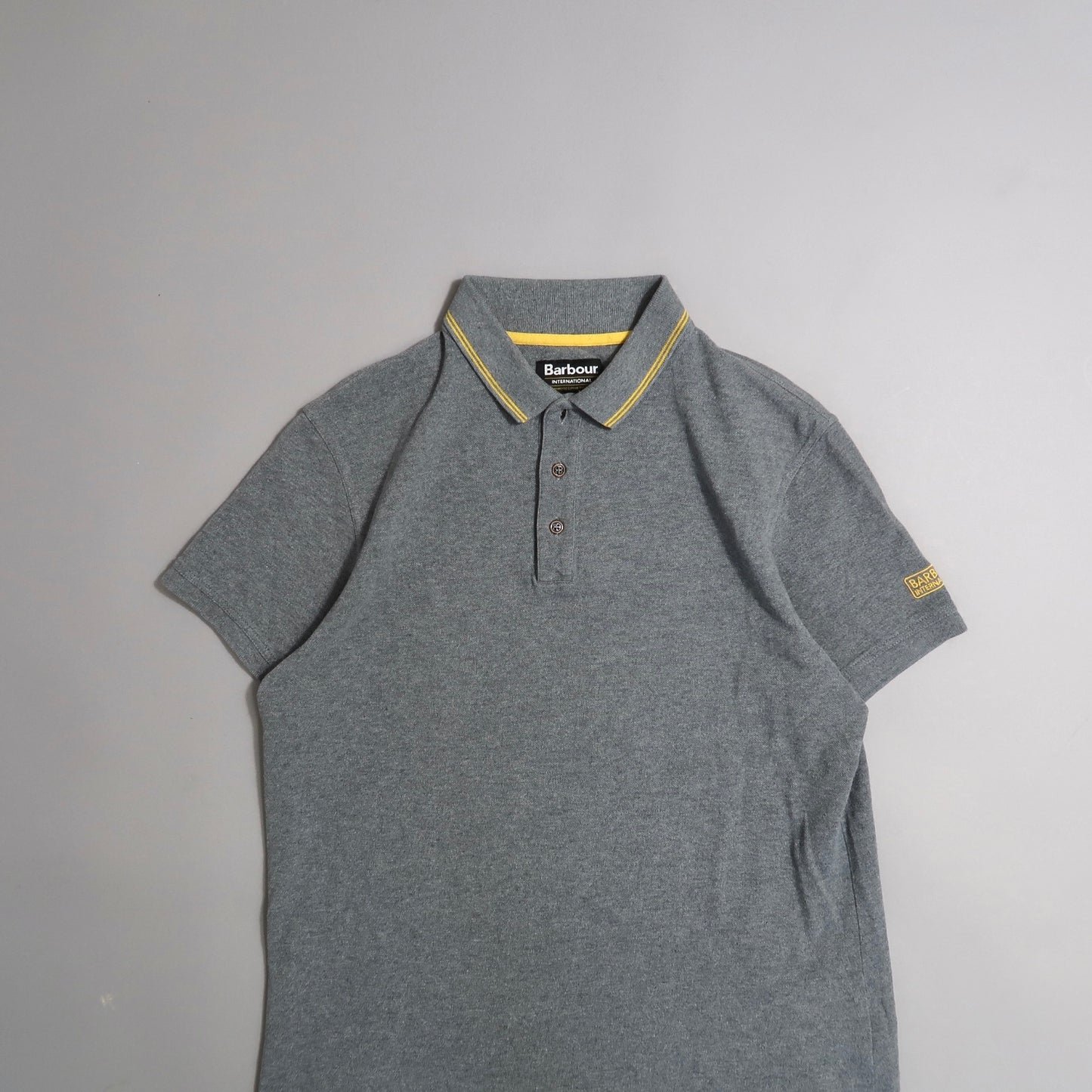 Gray polo shirt with yellow collar trim, on a plain background.