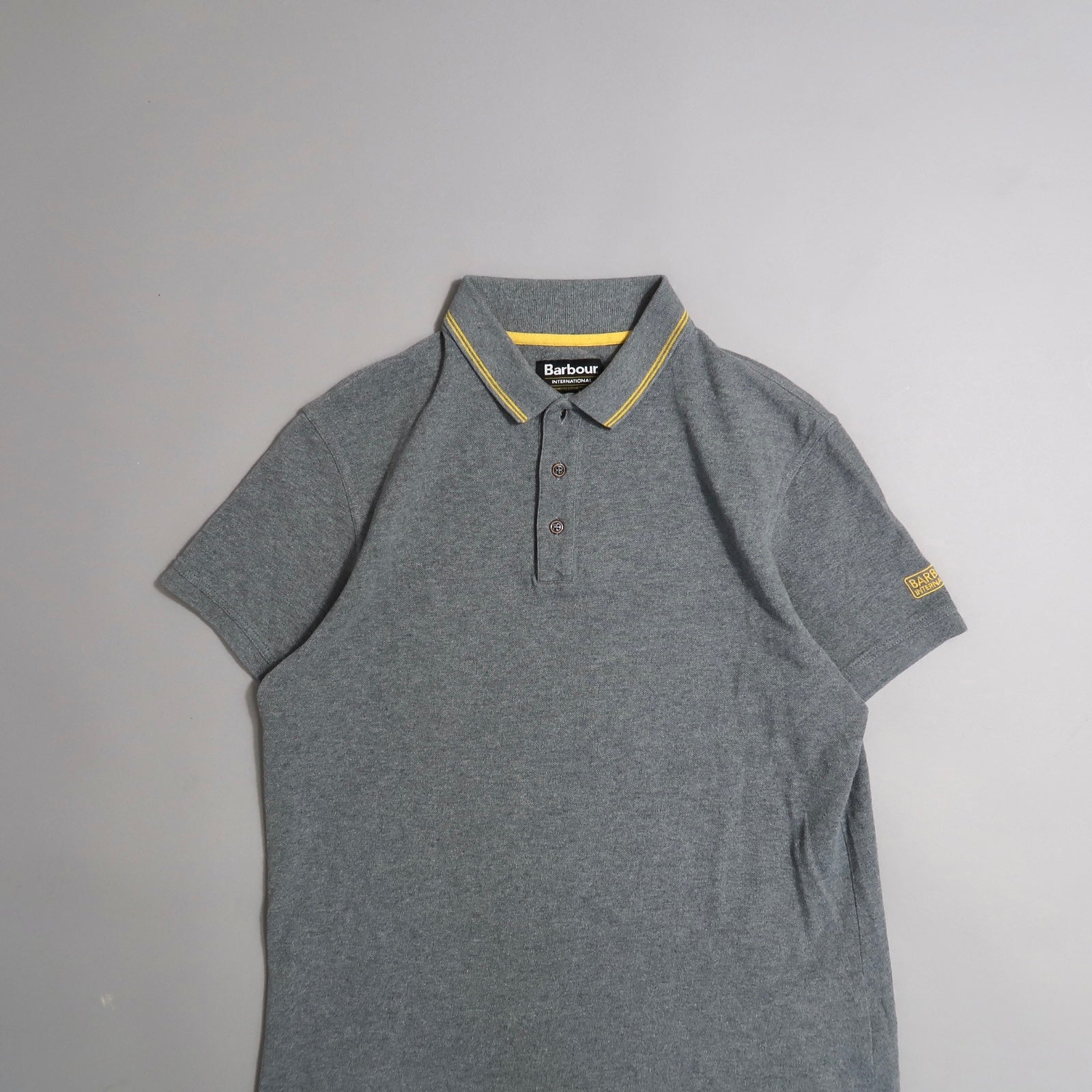 Gray polo shirt with yellow collar trim, on a plain background.
