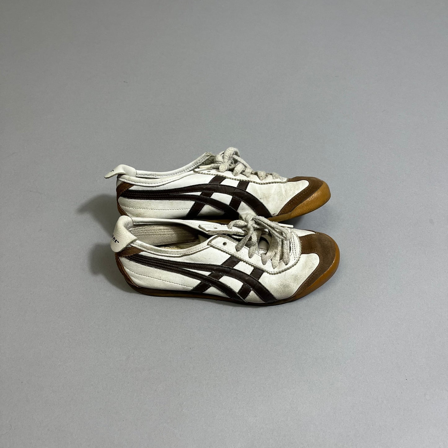 White and brown sneakers with black stripes on a gray background.