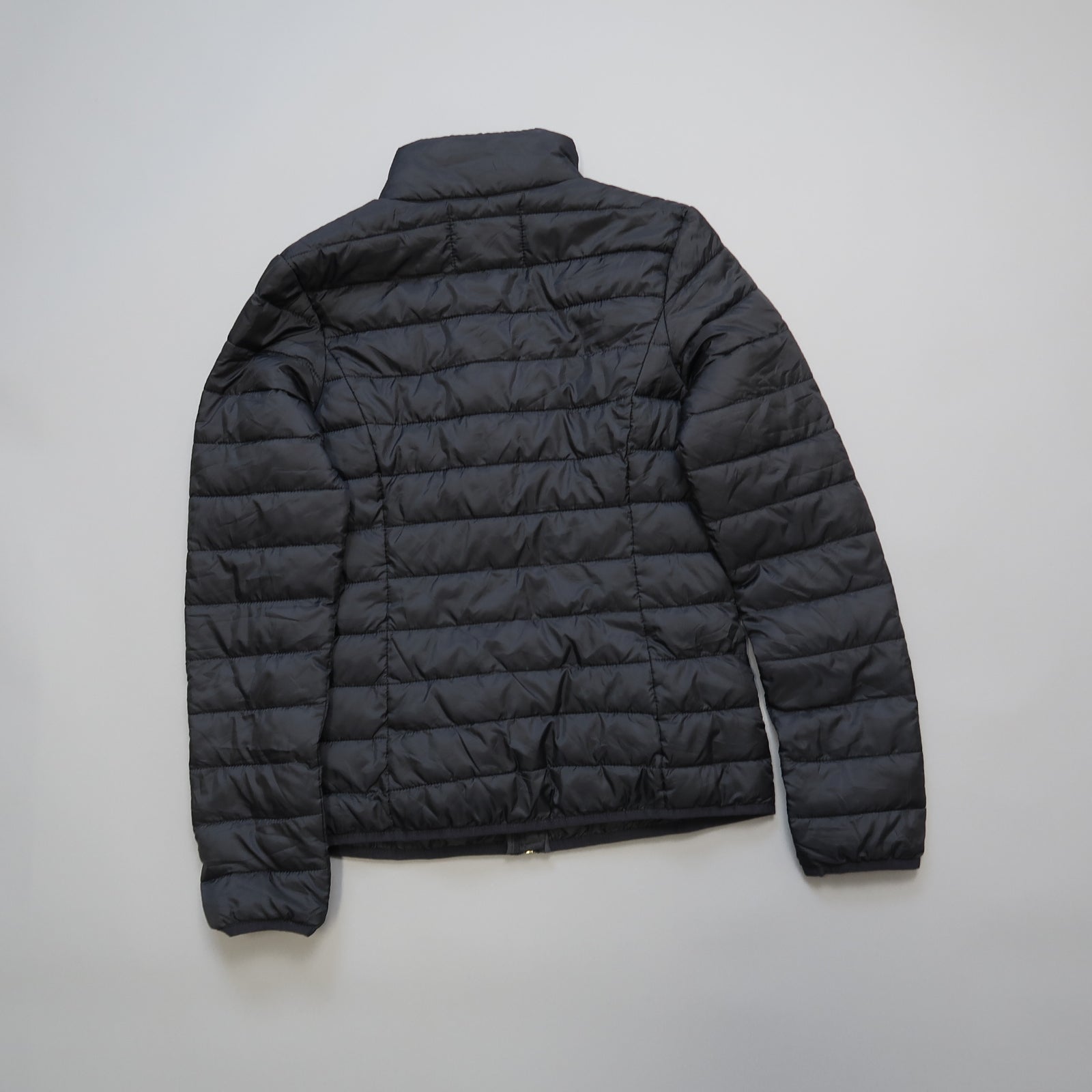Black puffer jacket laid flat on a light background.