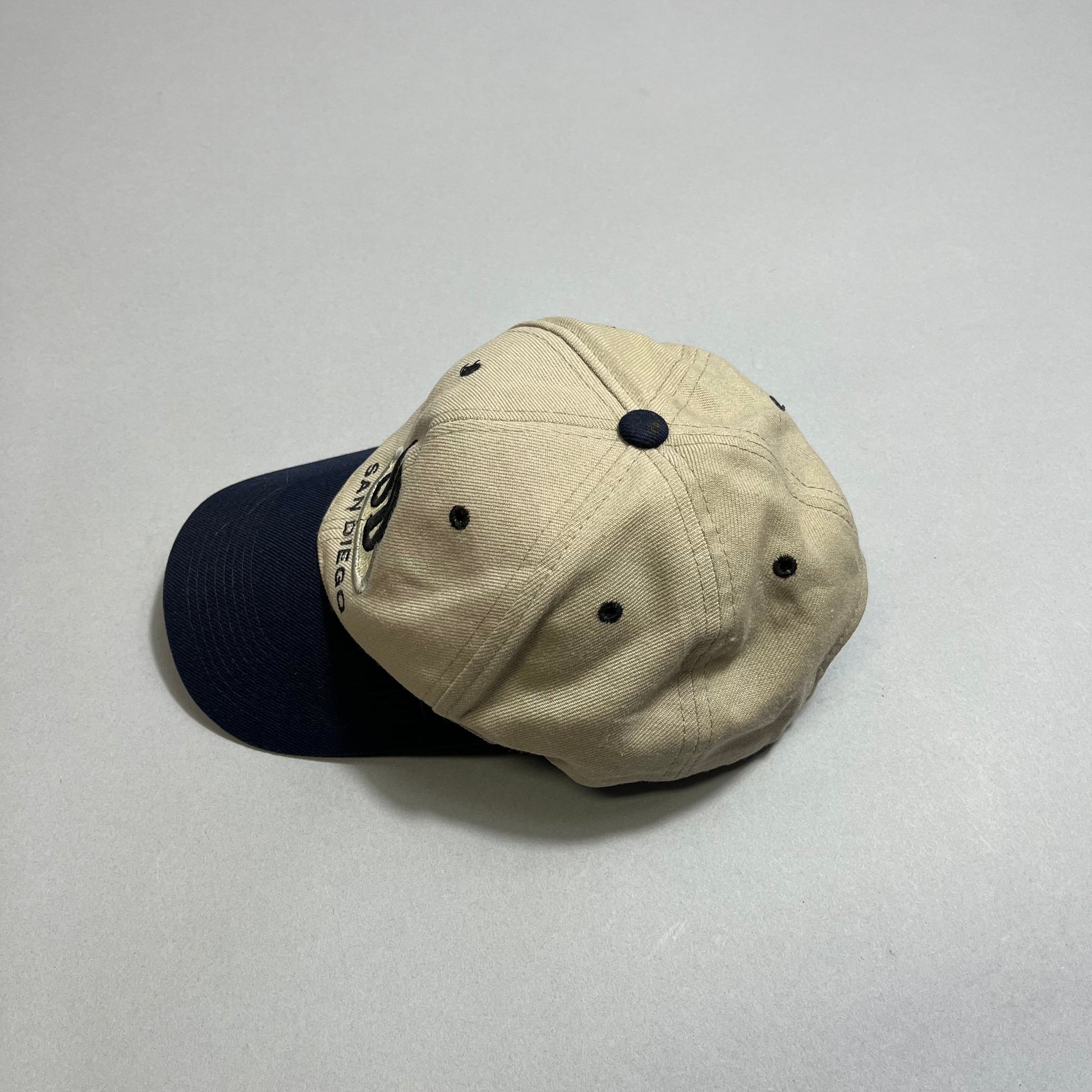 Tan baseball cap with a navy blue brim on a neutral background.