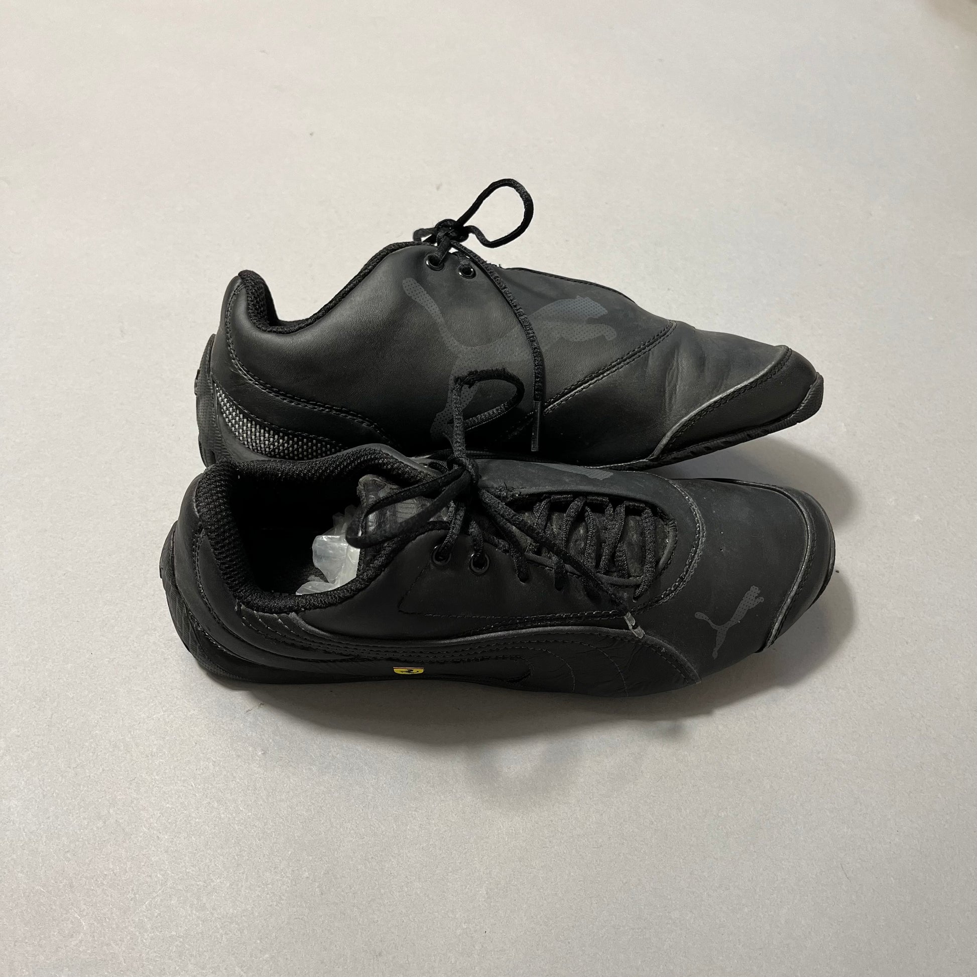 Pair of black Puma sneakers on a gray surface.