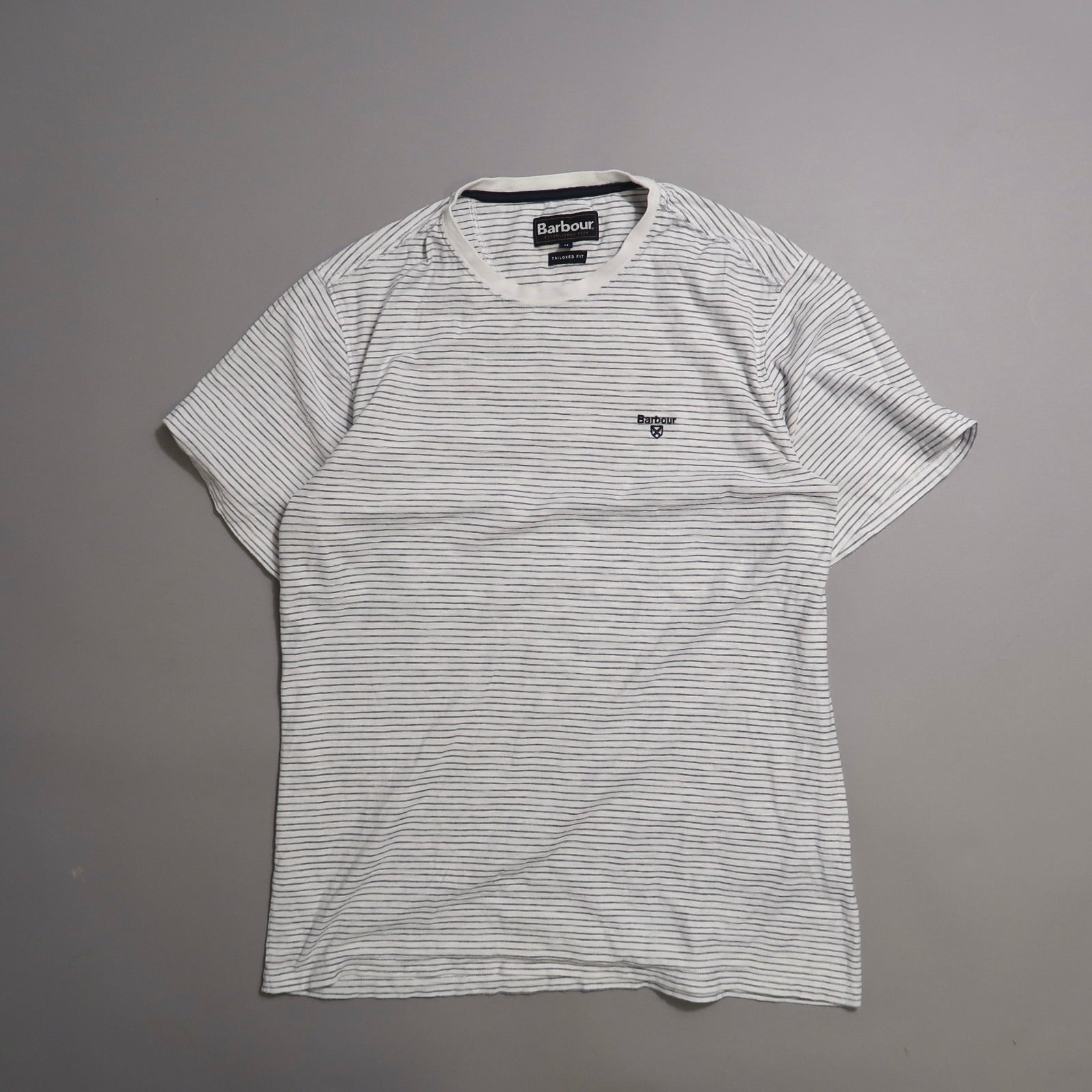Striped white T-shirt with logo on chest, laid flat against a gray background.