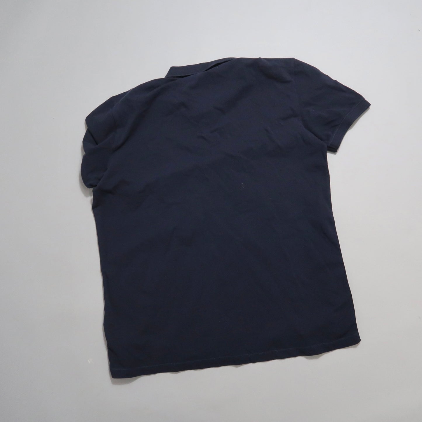 Back view of a navy blue short-sleeve polo shirt on a light surface.