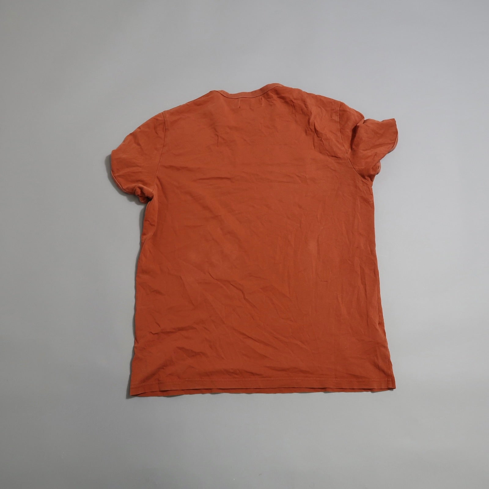 Wrinkled orange T-shirt lying flat on a light grey surface.