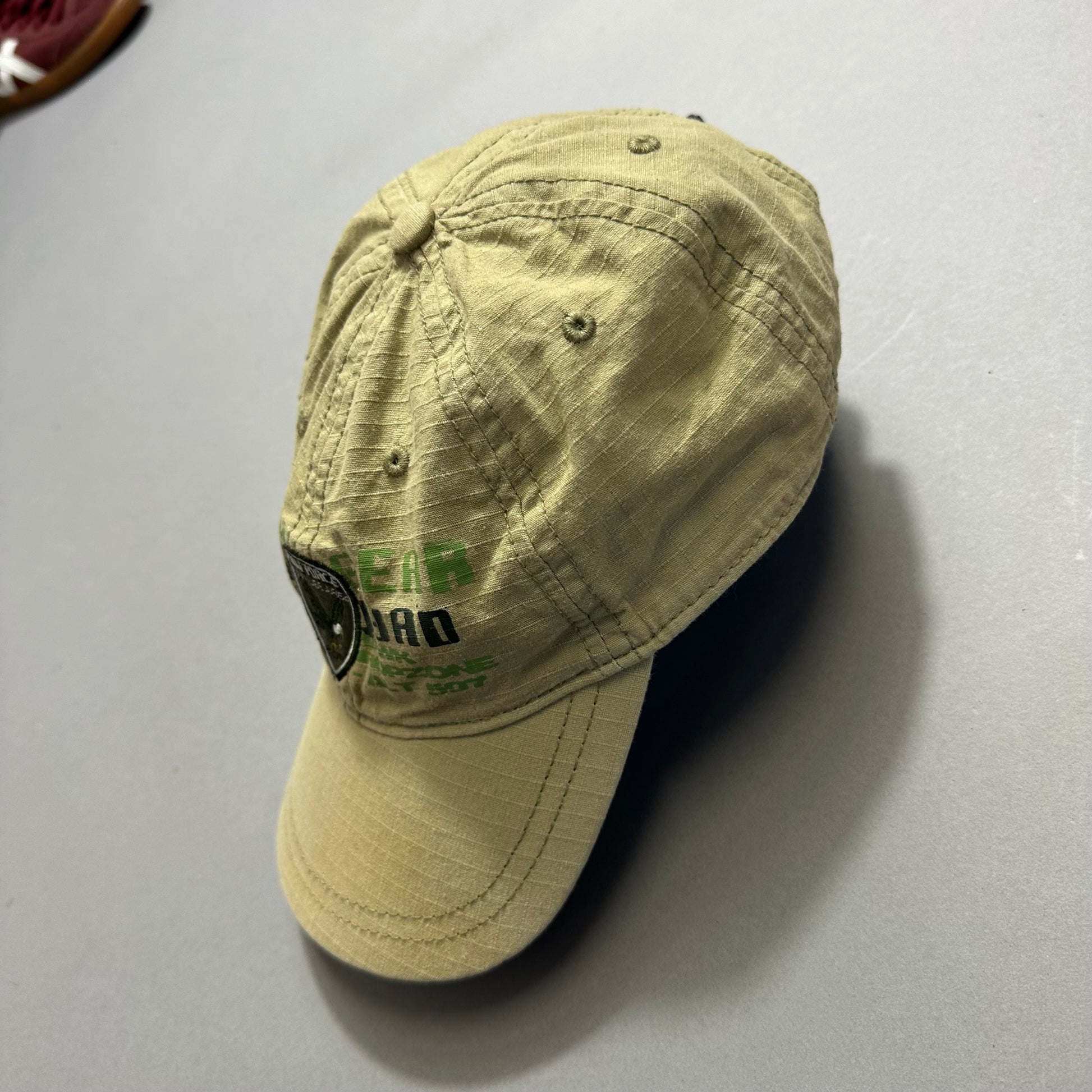 Tan cap with stitched shield logo and green text on the side.