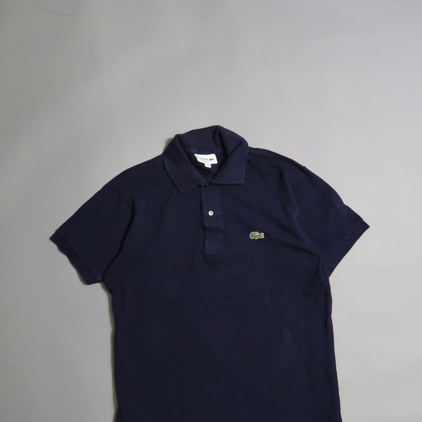 Navy polo shirt with embroidered green crocodile logo on gray background.