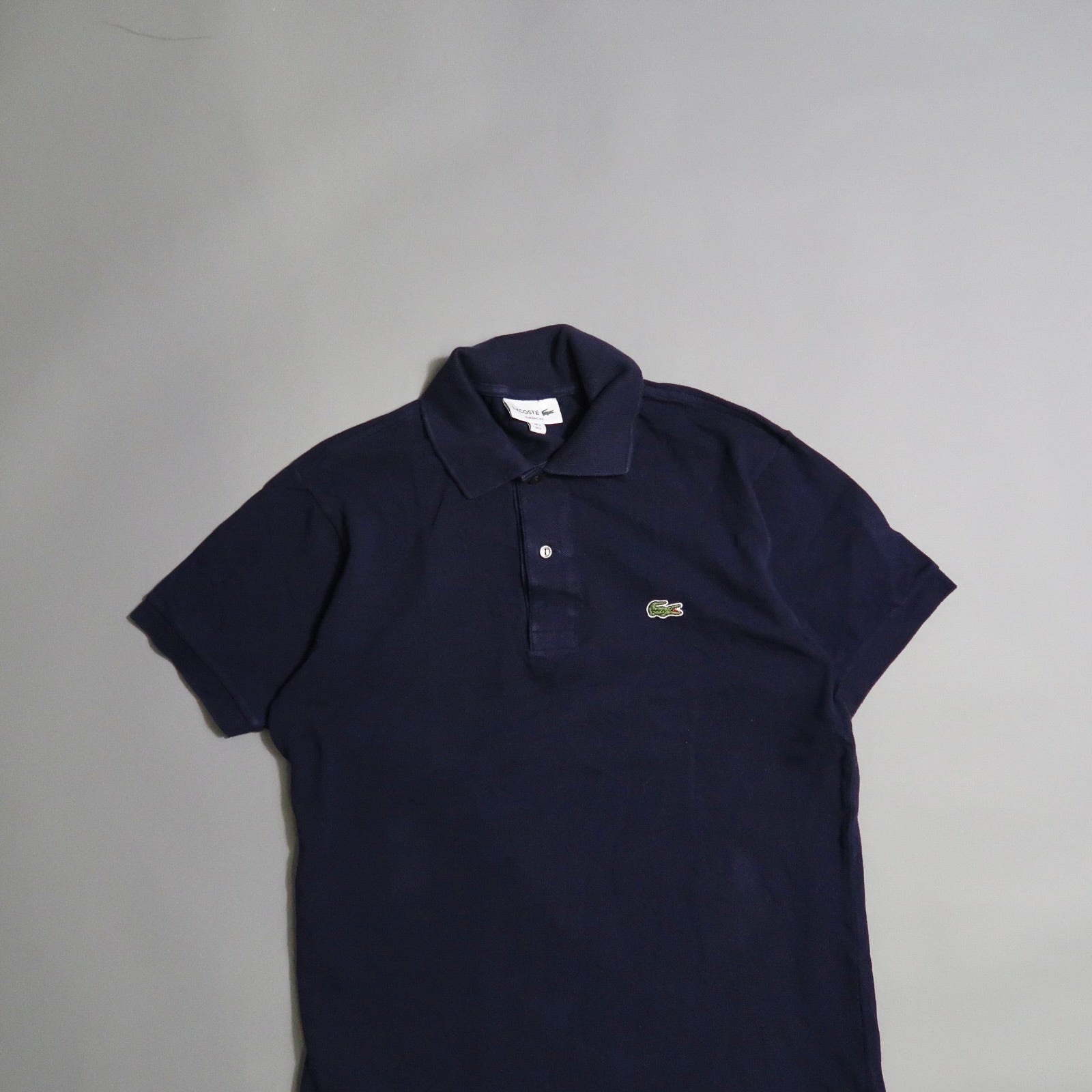 Navy polo shirt with embroidered green crocodile logo on gray background.