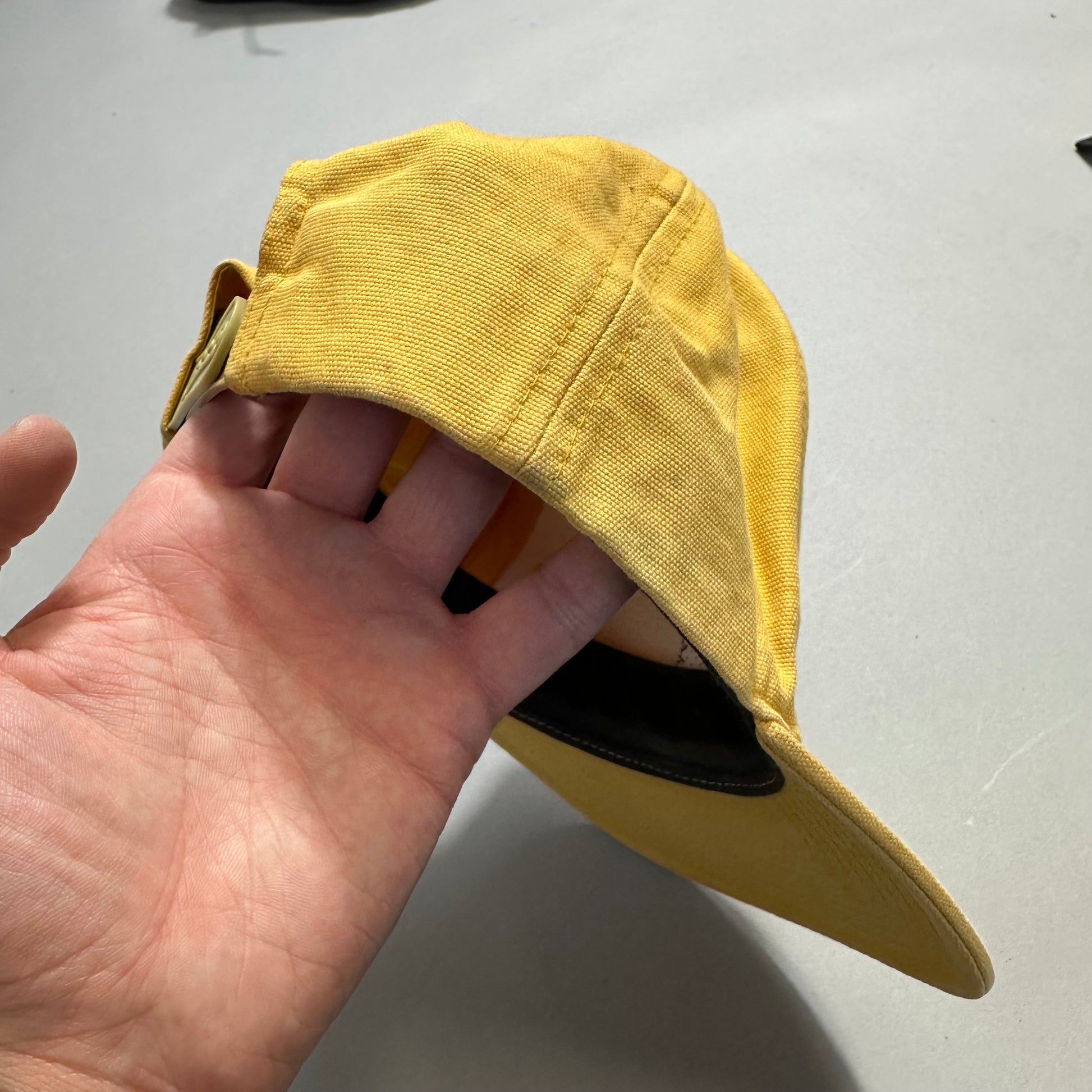 Hand holding a yellow cap with visible buckle and brim.