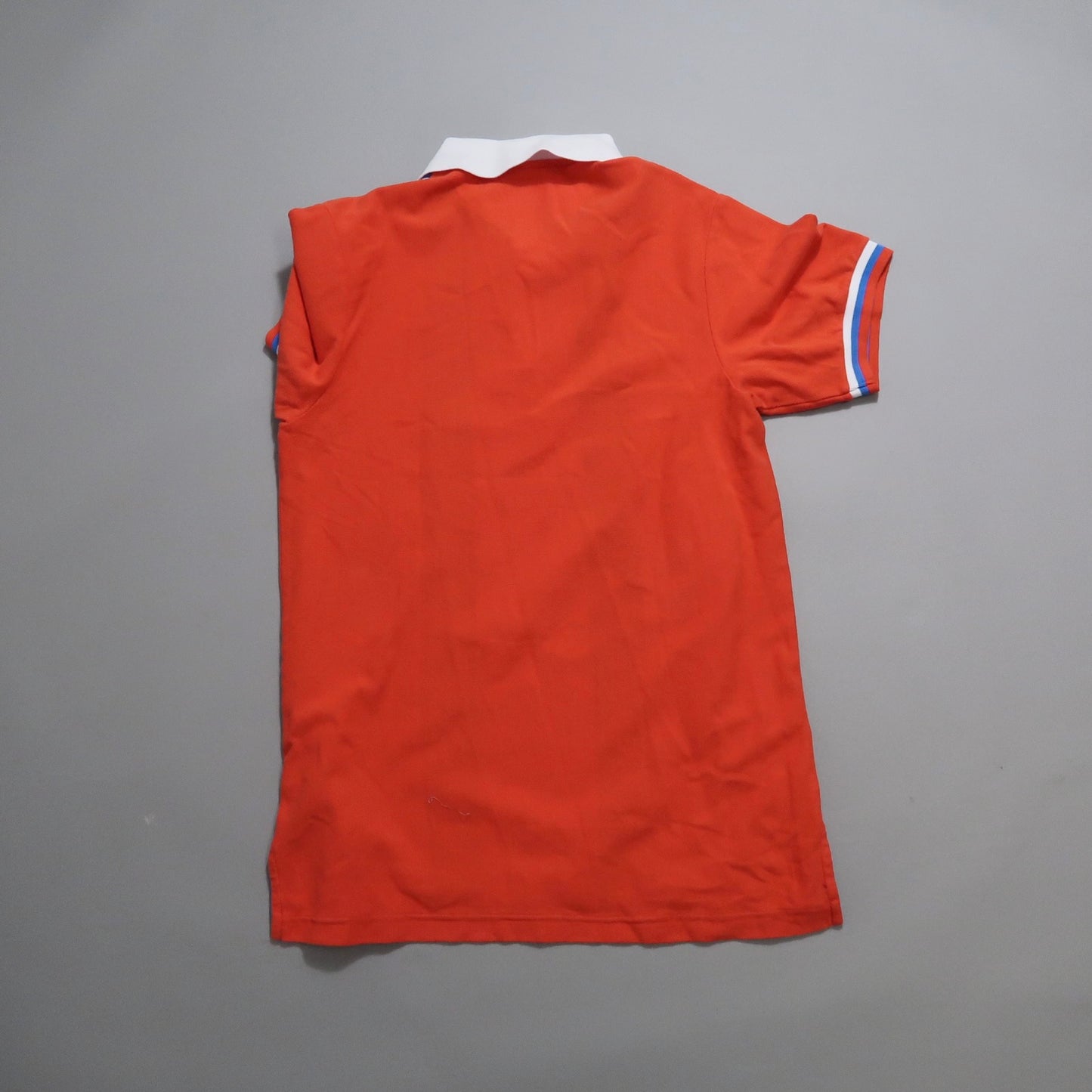 Back view of a red polo shirt with white collar on a gray background.