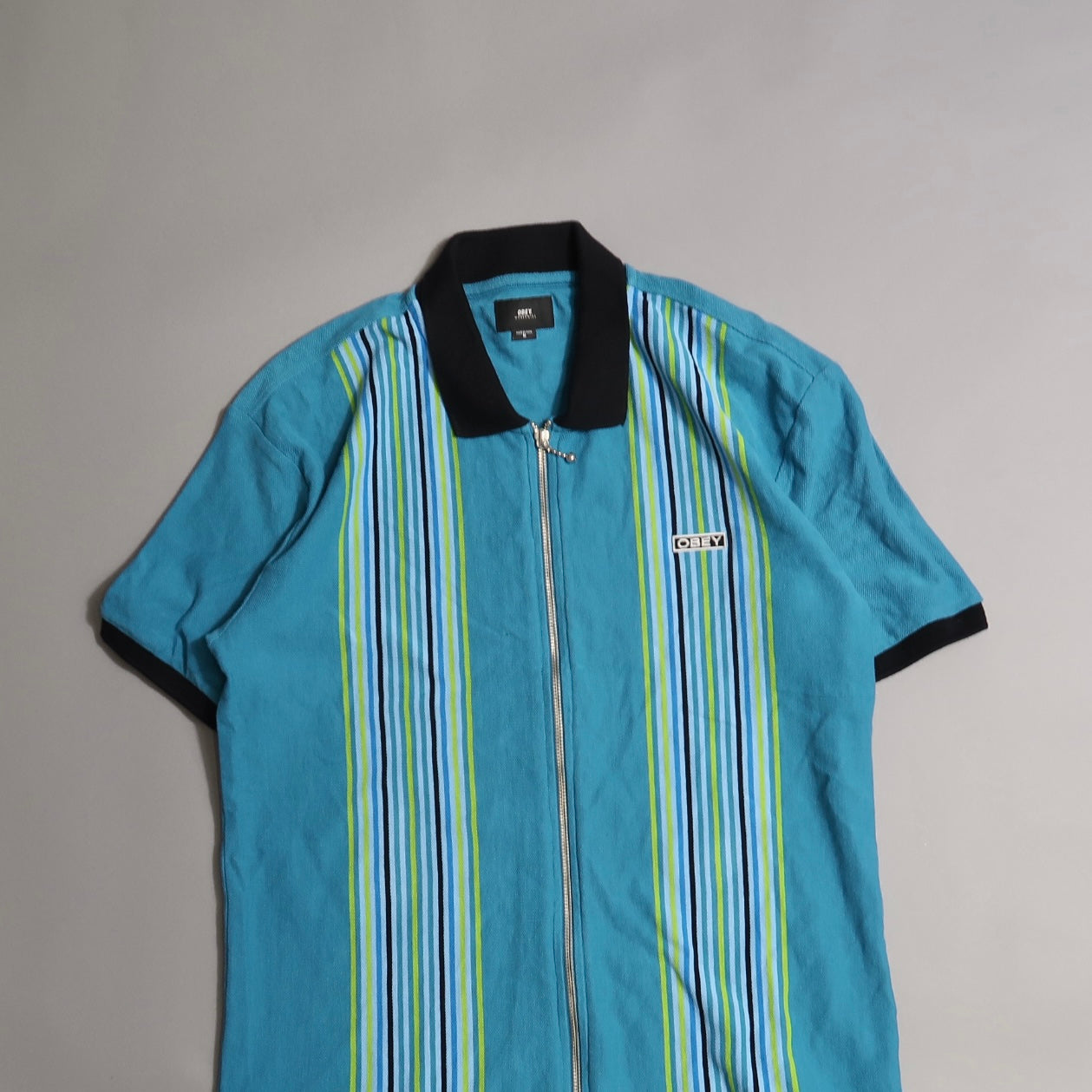 Blue collared shirt with colorful vertical stripes and a zipper.