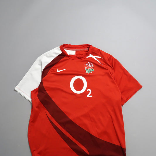 Red sports jersey with O2 logo and rose emblem on gray background.