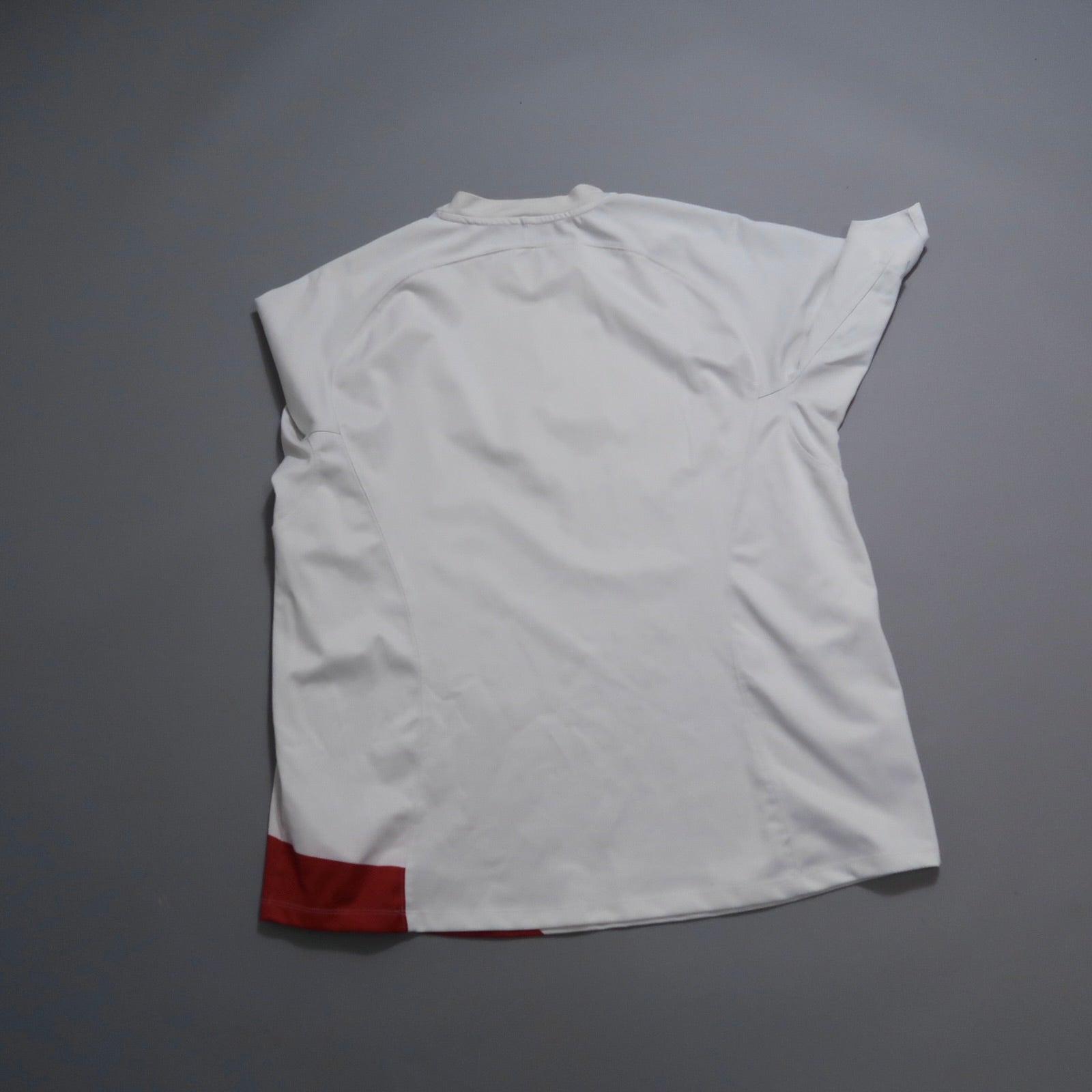 White shirt with red accents laid flat on a gray surface.