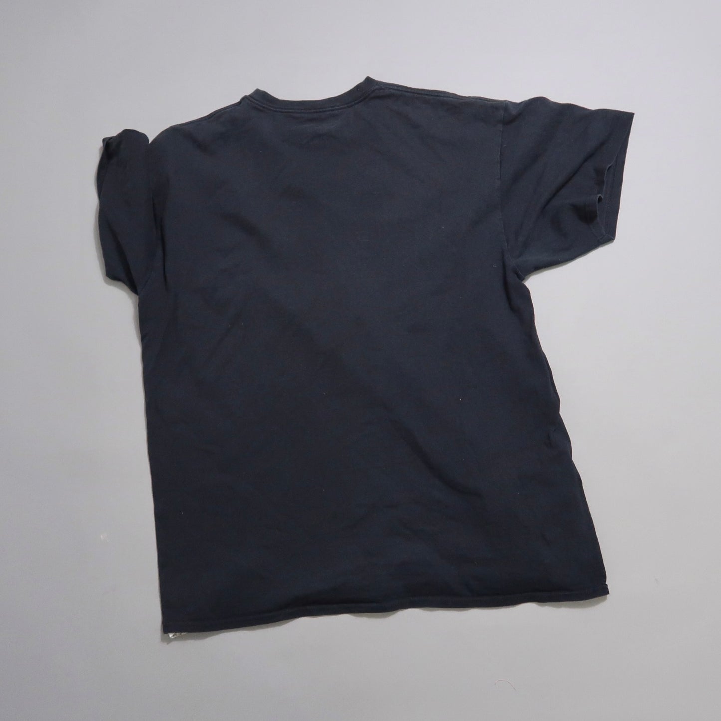 Back view of a plain black T-shirt on a gray background.