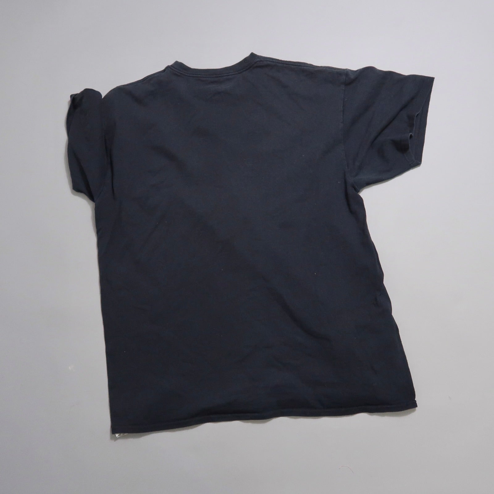 Back view of a plain black T-shirt on a gray background.