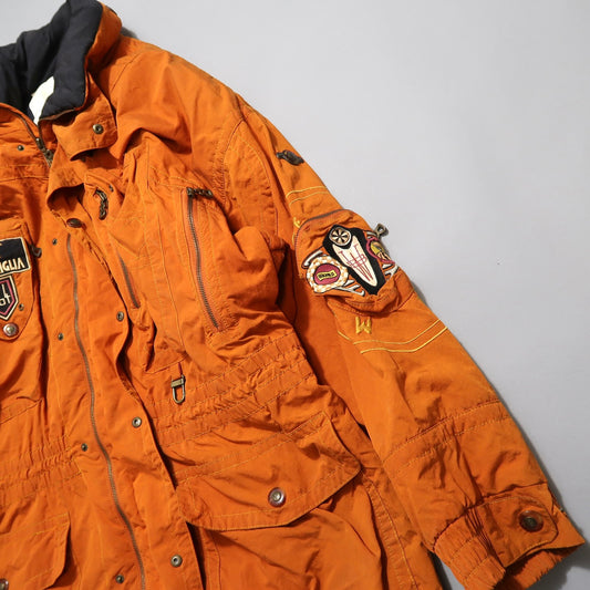 Orange jacket with multiple patches and pockets on a gray background.